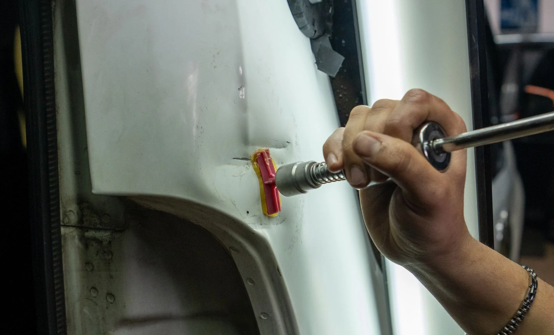 Paintless dent repair technician using a glue-pull tool on a car panel